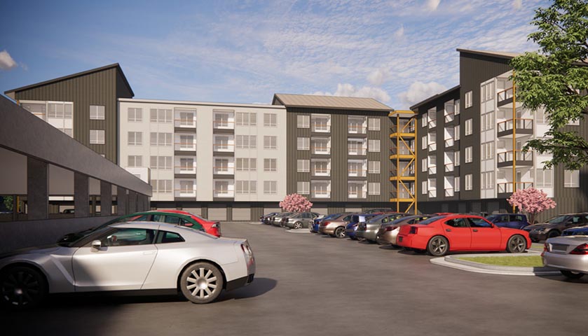 Modern multifamily apartment complex with parking lot, vehicles, and landscaping under blue sky.